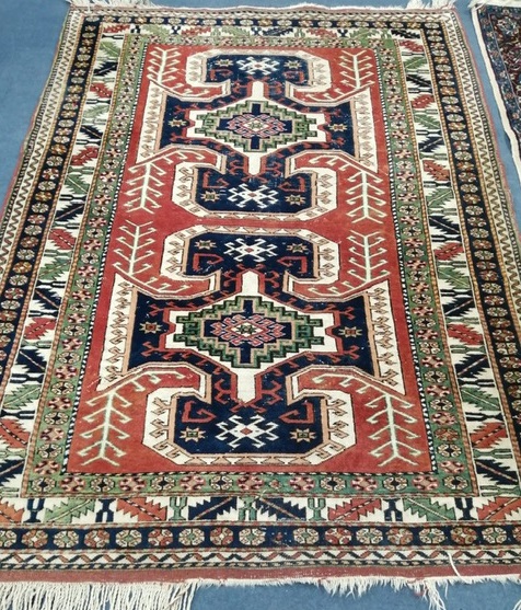 A Caucasian red ground rug with two hooked medallions and nine-row border 280 x 187cm